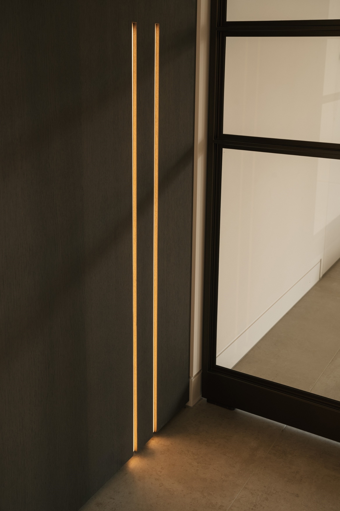 Twee ledstrips in de wand die exact aansluiten op de middenstijl van de stalen deuren, strakk interieurbouw